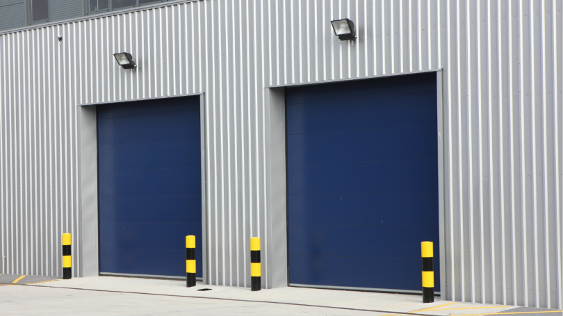 Warehouse exterior with blue roller shutter doors and safety bollards